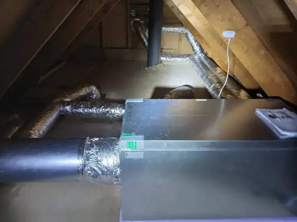 Ventilationssystem i en vind med isolerade rör och en aggregatbox. Systemet är installerat för att hantera kallras och säkerställa god luftkvalitet.