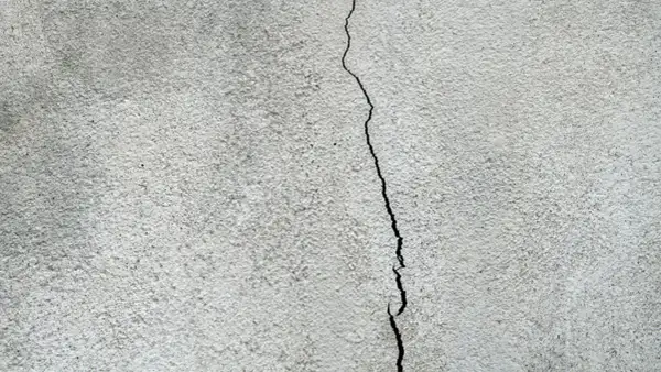 En spricka löper genom en grå, putsad fasad. Dags att laga sprickor i putsad fasad för att skydda huset.