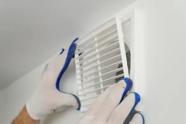 Händer med handskar rengör ett ventilationsgaller för att förbättra dammigt hemma ventilation.