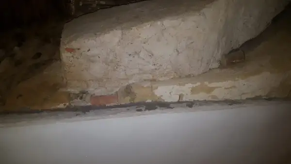 Detaljerad vy av en gammal murstock som är i behov av att riva murstock. Synliga tegelstenar och puts.