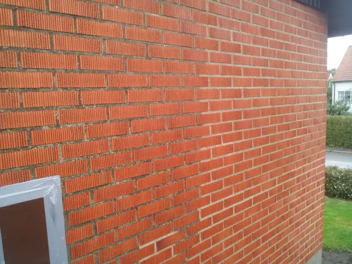 En röd tegelfasad med vertikala spår i tegelstenarna. En del av en fönsterkarm syns i nedre vänstra hörnet.